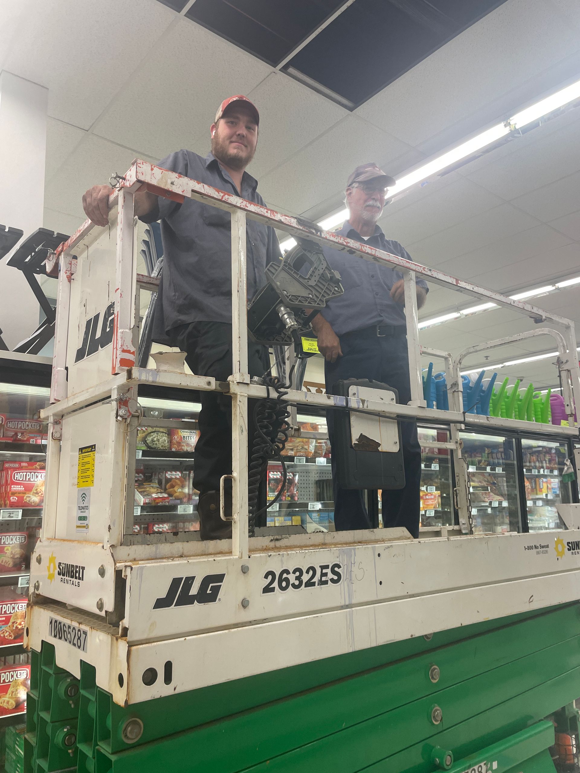 Two men are standing on a scissor lift in a store.