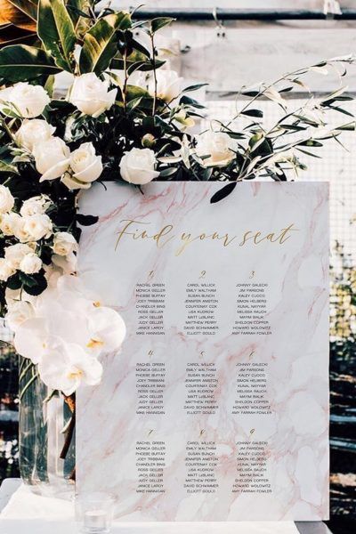 A seating chart for a wedding is surrounded by white flowers.