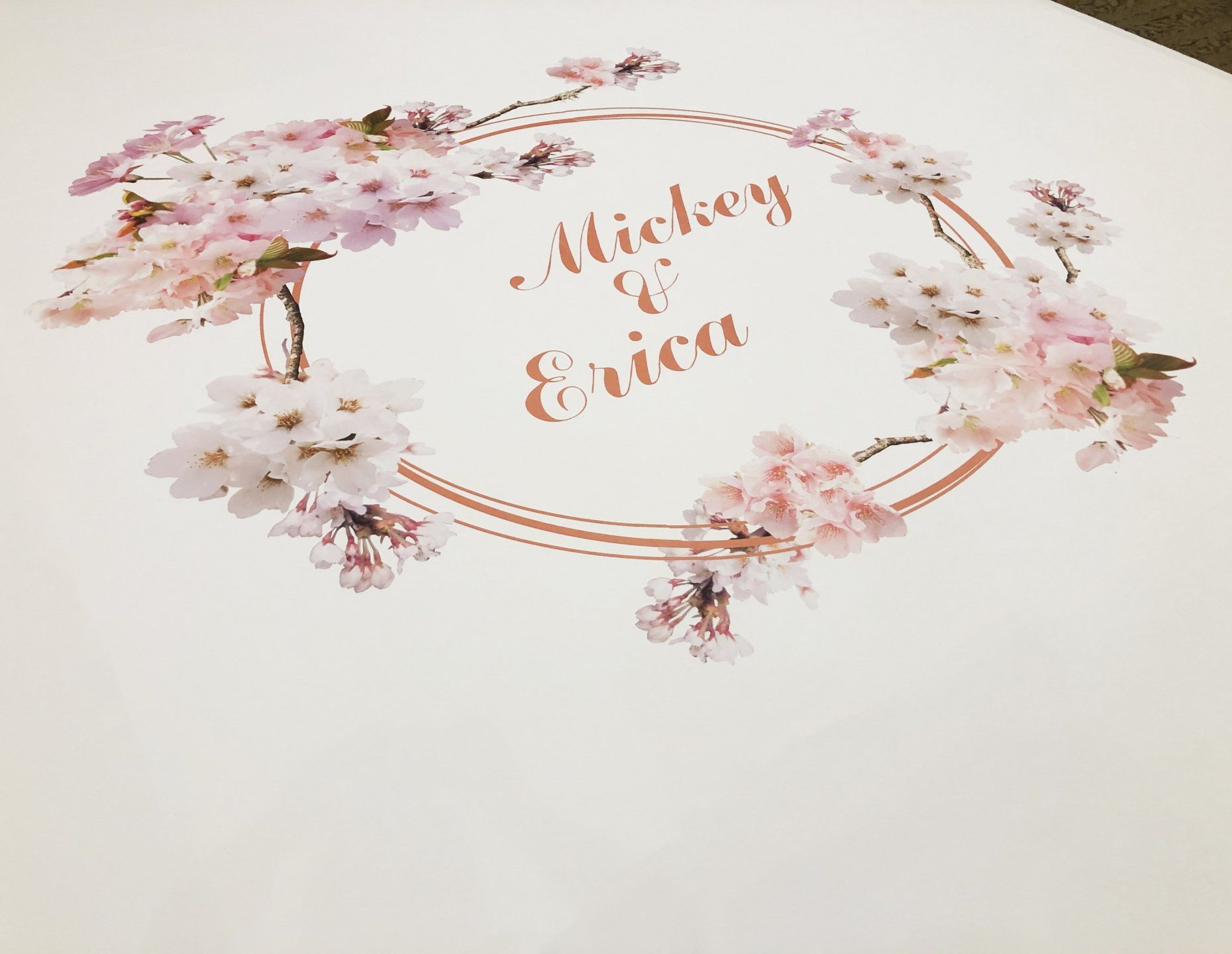 A wedding invitation with a wreath of flowers and the names mickey and erica