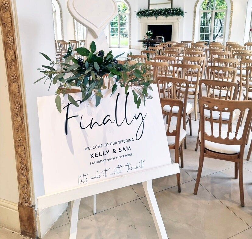 A sign that says finally is on a white easel in front of rows of chairs.