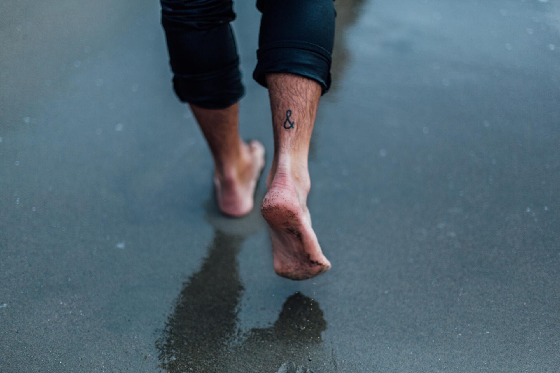 Man walking on a beach barefoot with tattoo on ankle