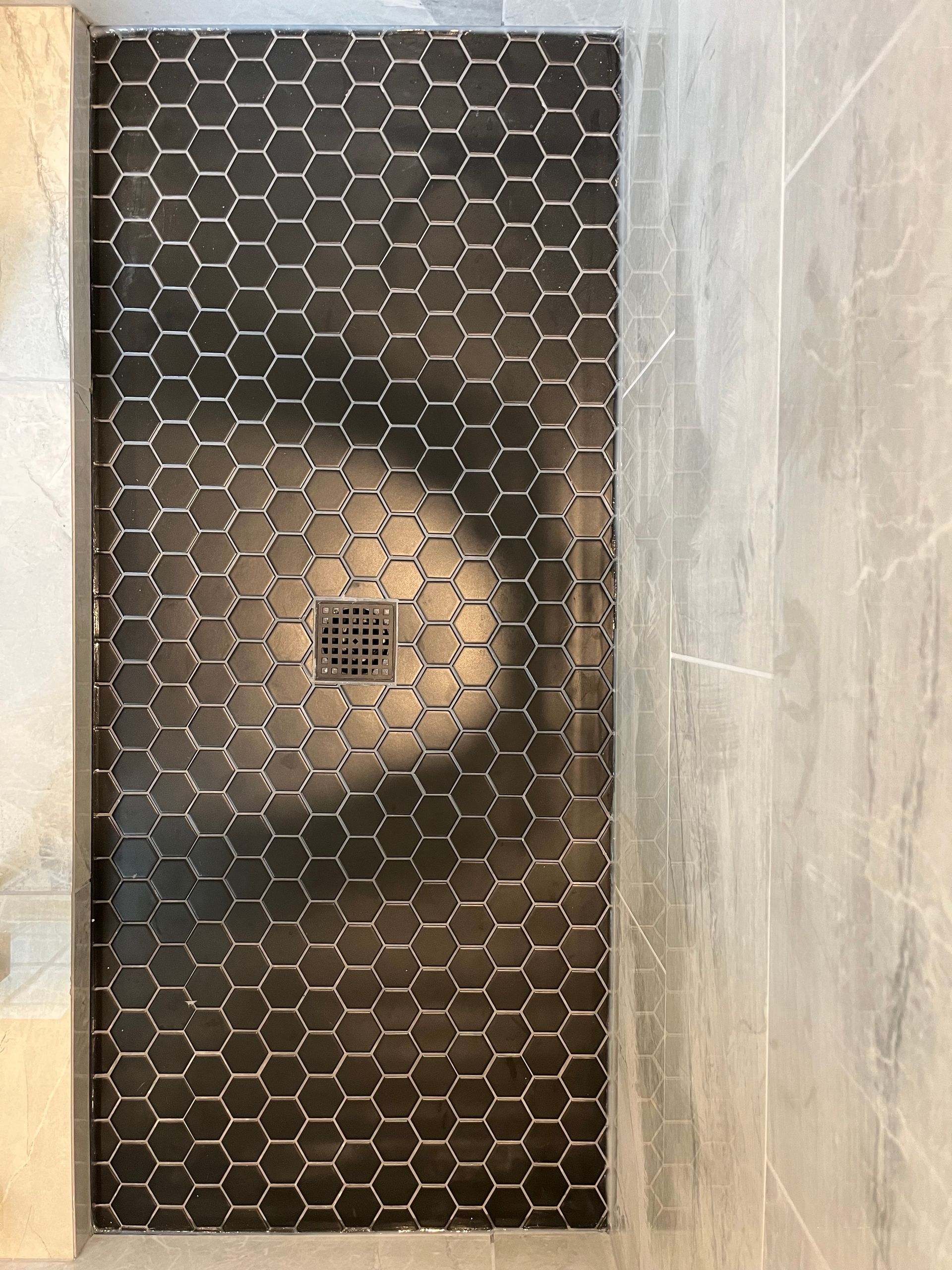 a shower stall with black hexagon tiles and a drain