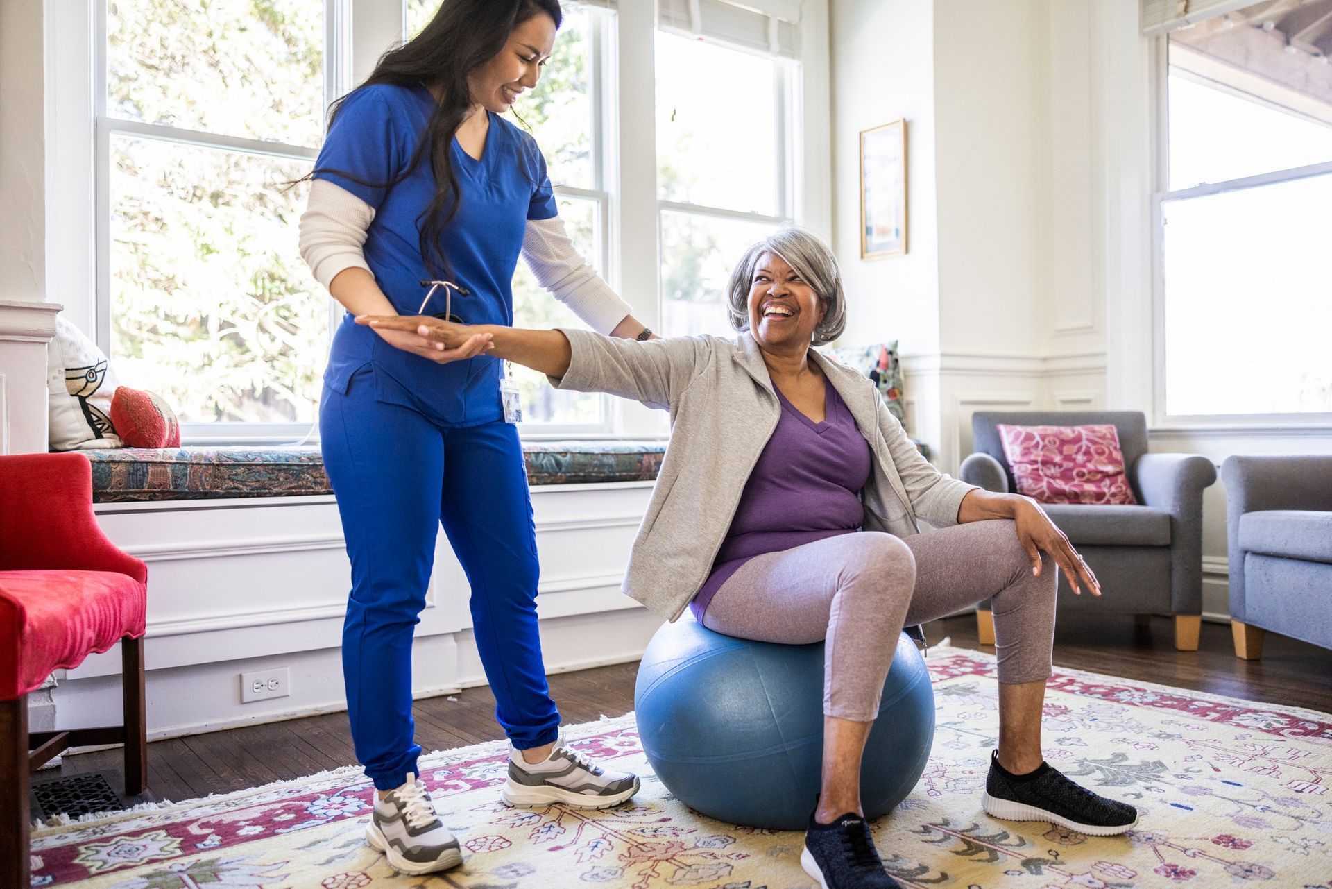 A nurse is helping an elderly woman sit on an exercise ball.