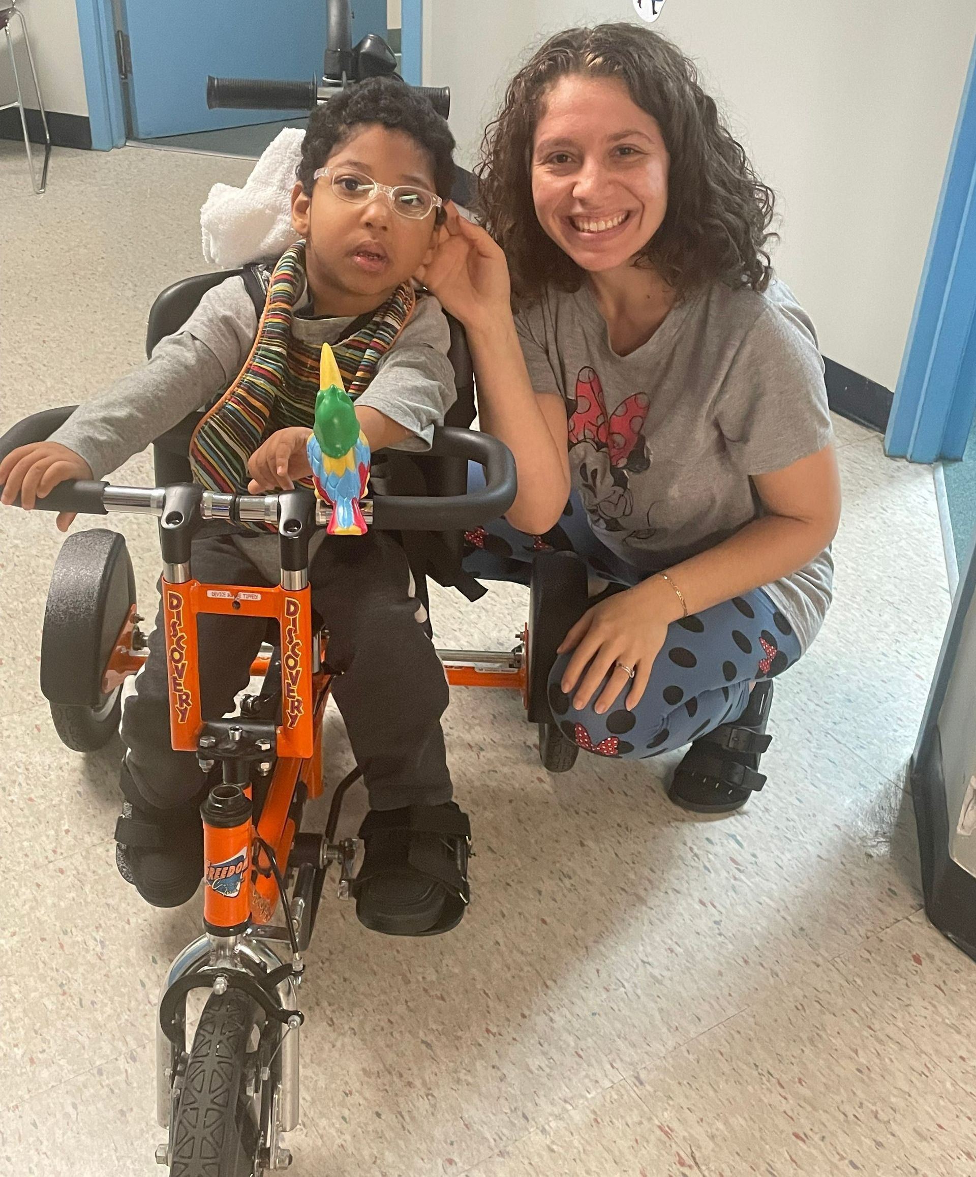 A woman is kneeling next to a child in a tricycle