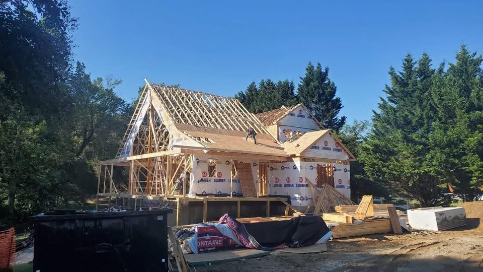 Partially built wooden house with exposed framing in a wooded area under a clear sky