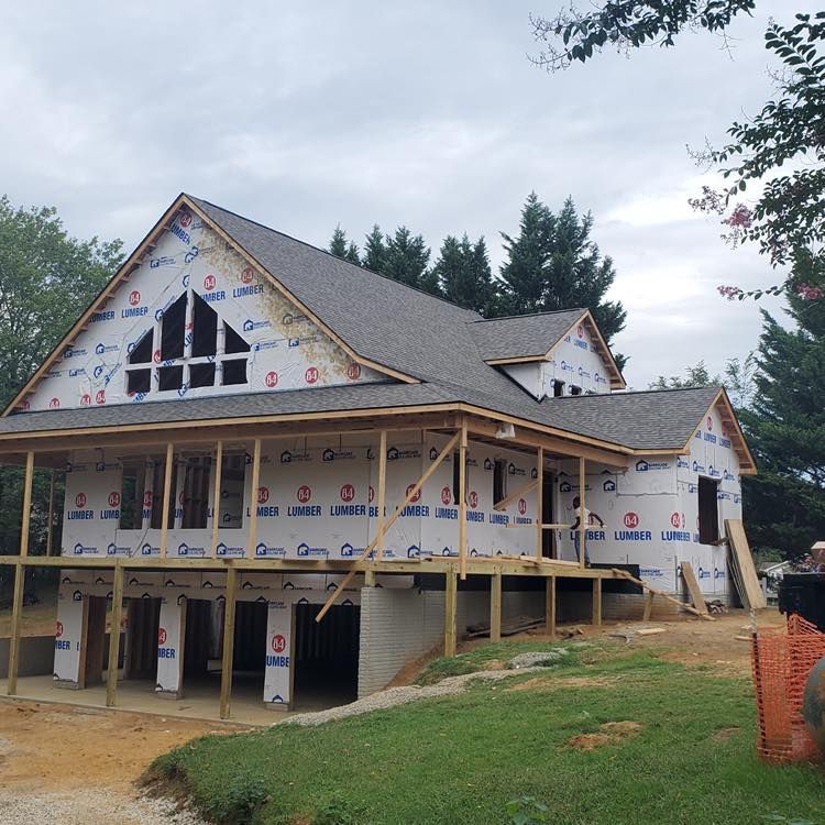 Partially built two-story house with wraparound porch, white siding, gray roof, and exposed framing