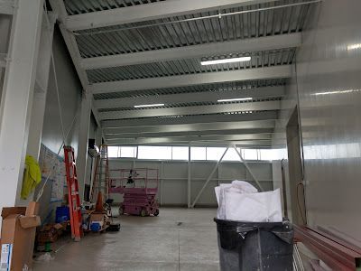 Interior of a commercial building under construction; white walls, metal beams, tools and debris visible.