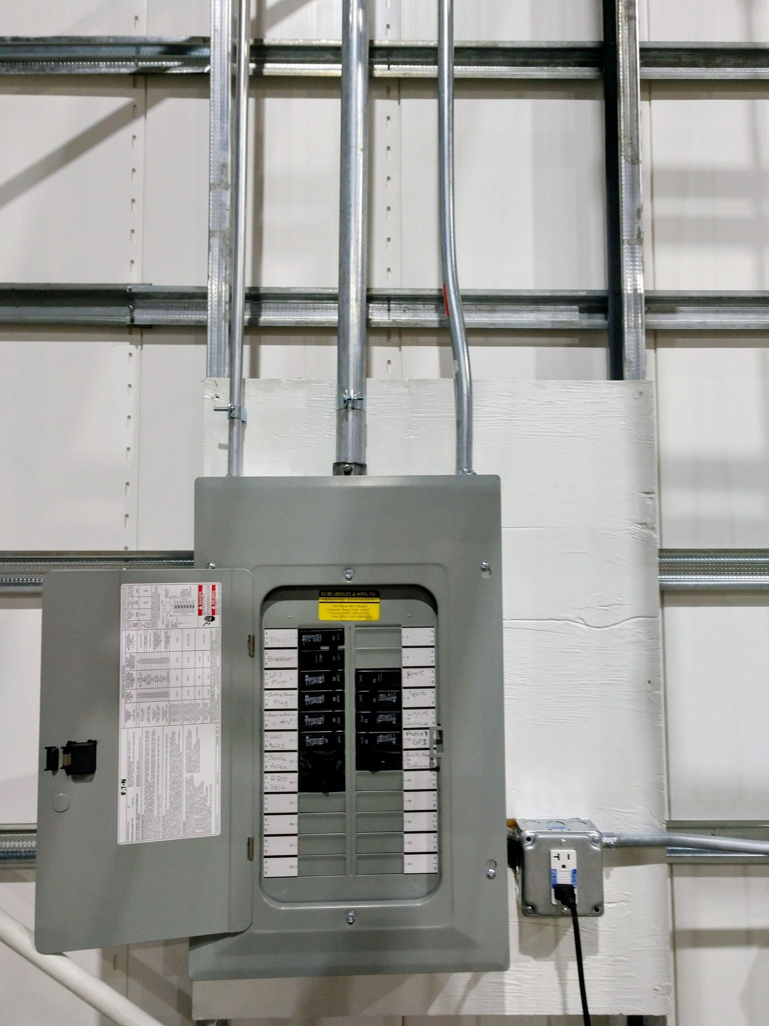 Electrical panel with conduit and an outlet installed on a white wall.