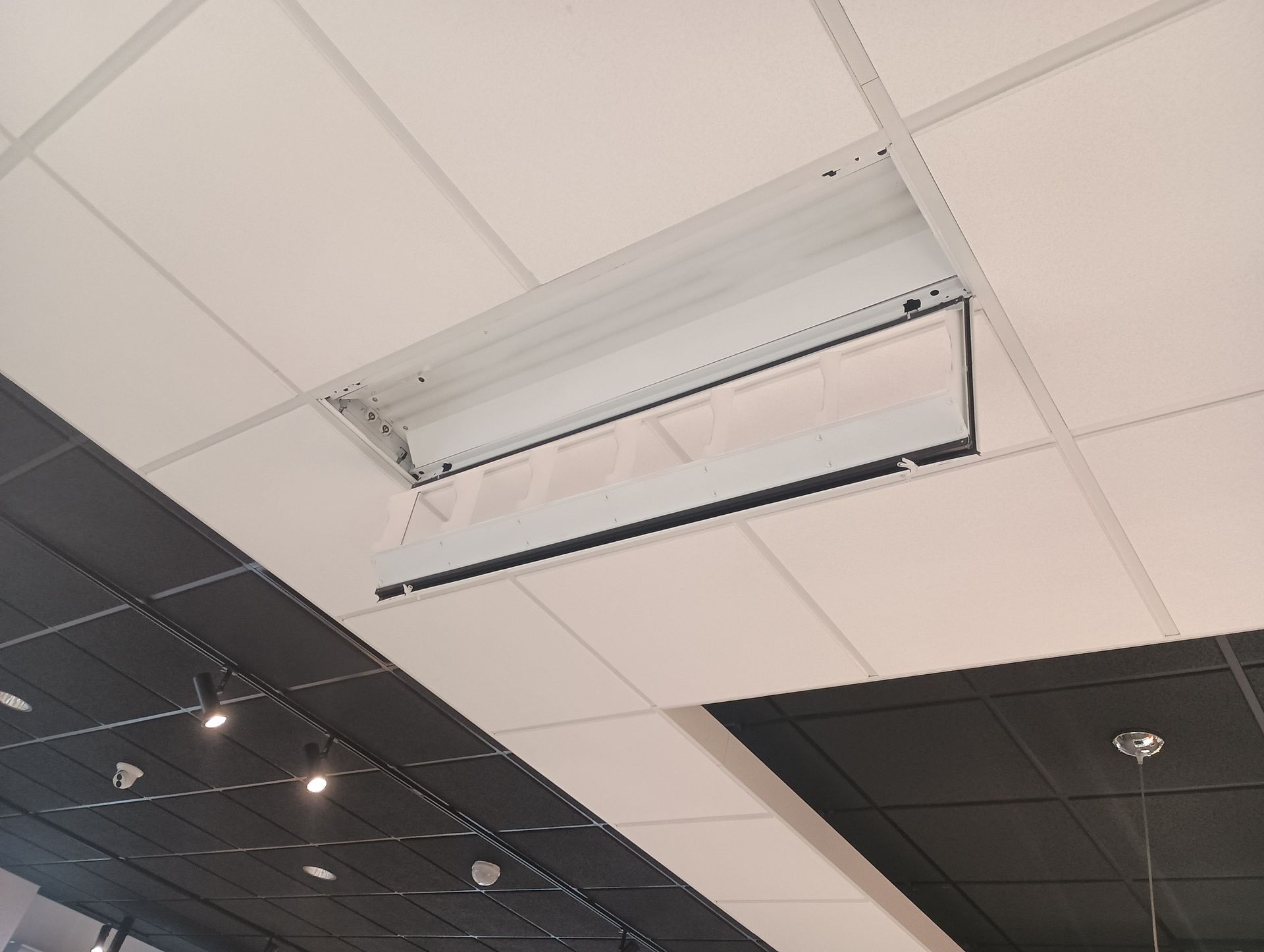 Ceiling with a removed tile revealing a fluorescent light fixture.