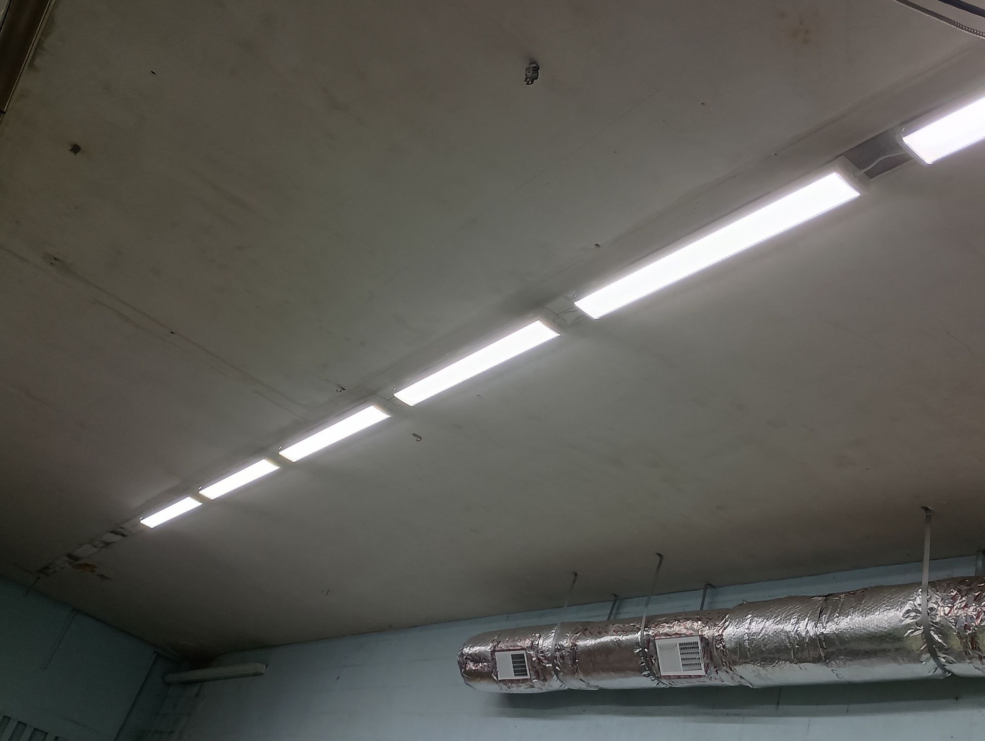 Fluorescent lights line a concrete ceiling in a room with blue walls and ductwork.
