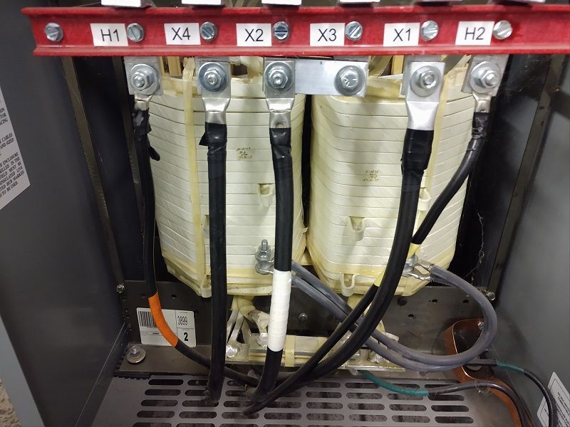 Close-up of electrical transformer connections. Six labeled terminals connected by wires and bolts, in a gray enclosure.