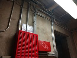 Red electrical control panels with metal conduit on a concrete wall.