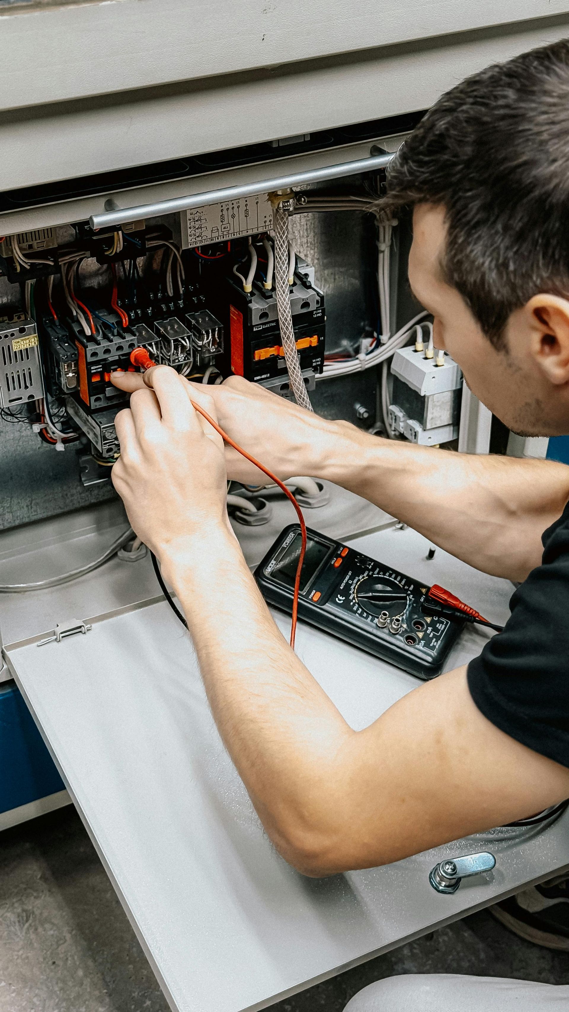 Technician wiring an open electrical panel with red and black cables on a workbench