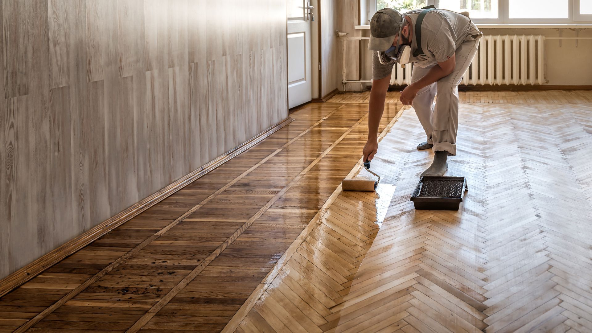A man is painting a wooden floor with a roller.