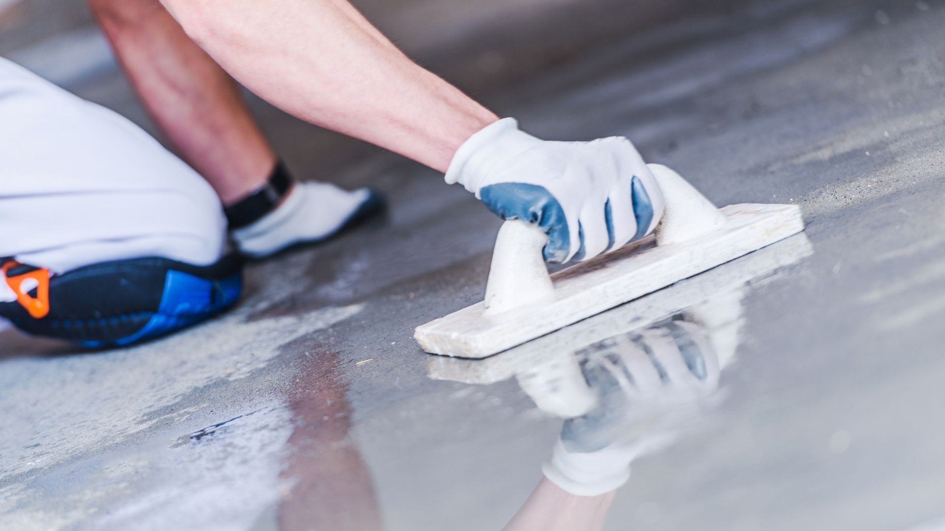 A person is using a trowel to smooth a concrete floor.