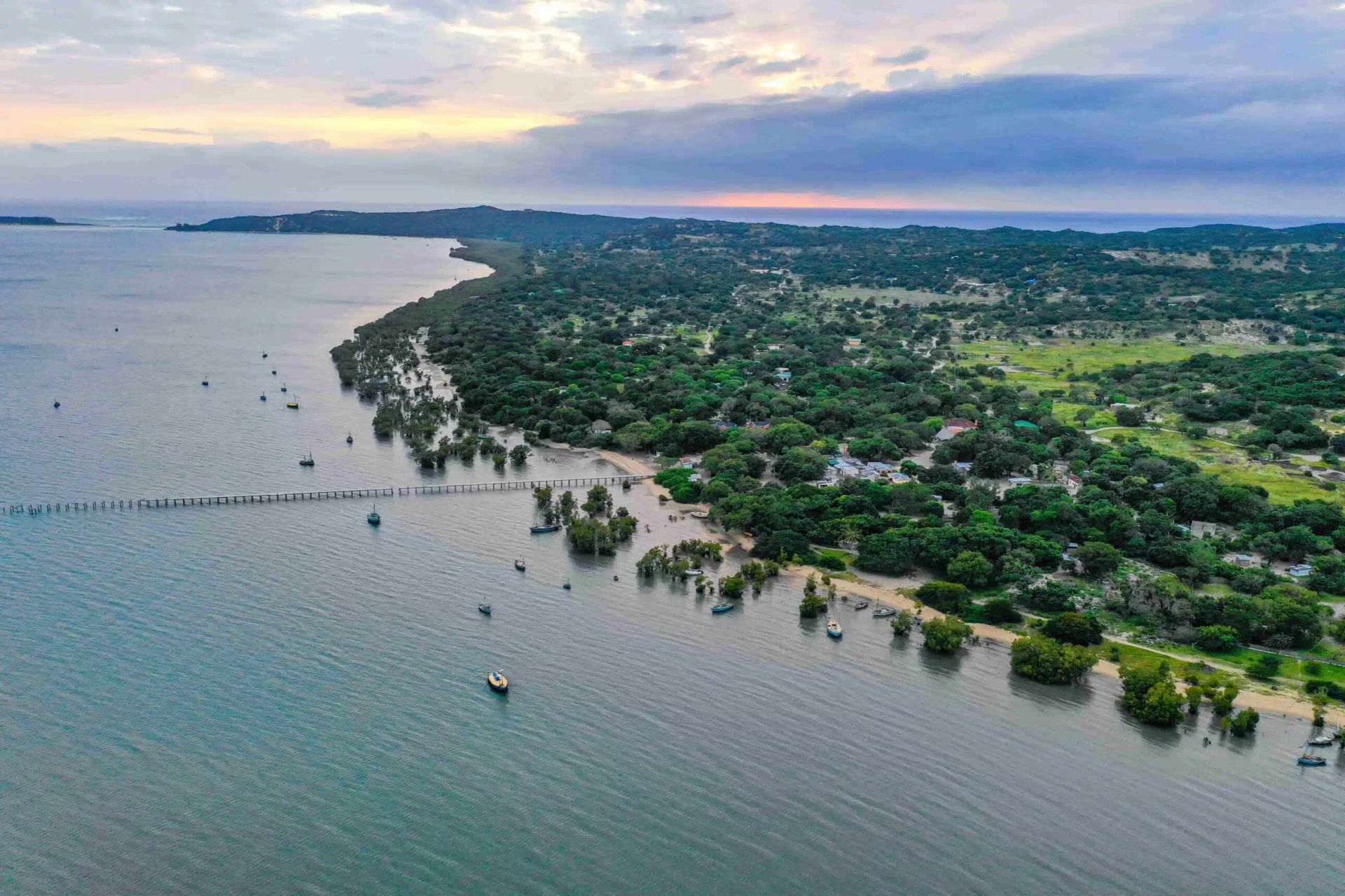 Aerial view of a coastal village with a long wooden pier extending into the water at sunset.