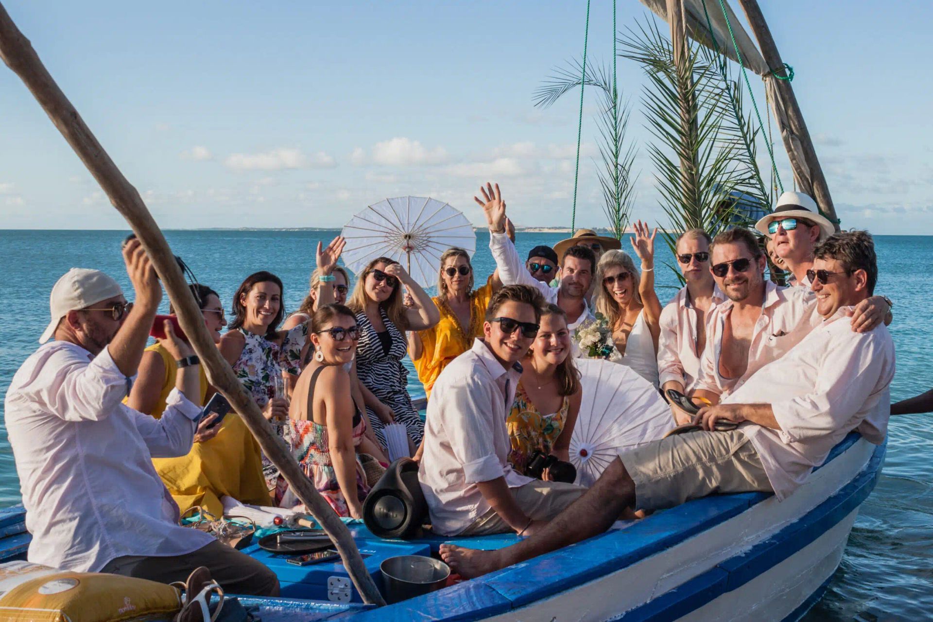 Group of people smiling on a sailboat at sea, with a Ferris wheel in the background.