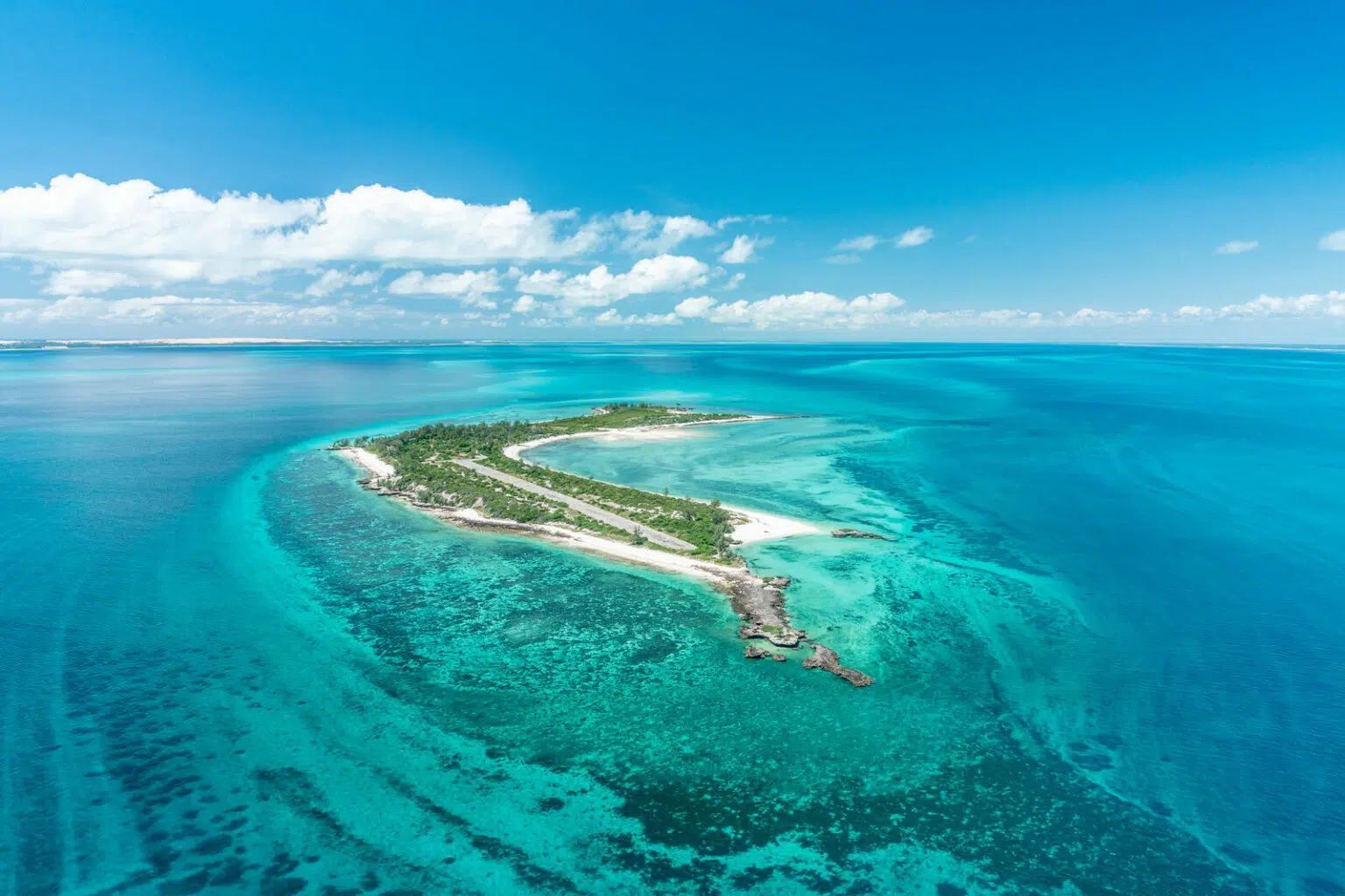 Aerial view of a small tropical island with turquoise water and coral reefs under a bright blue sky