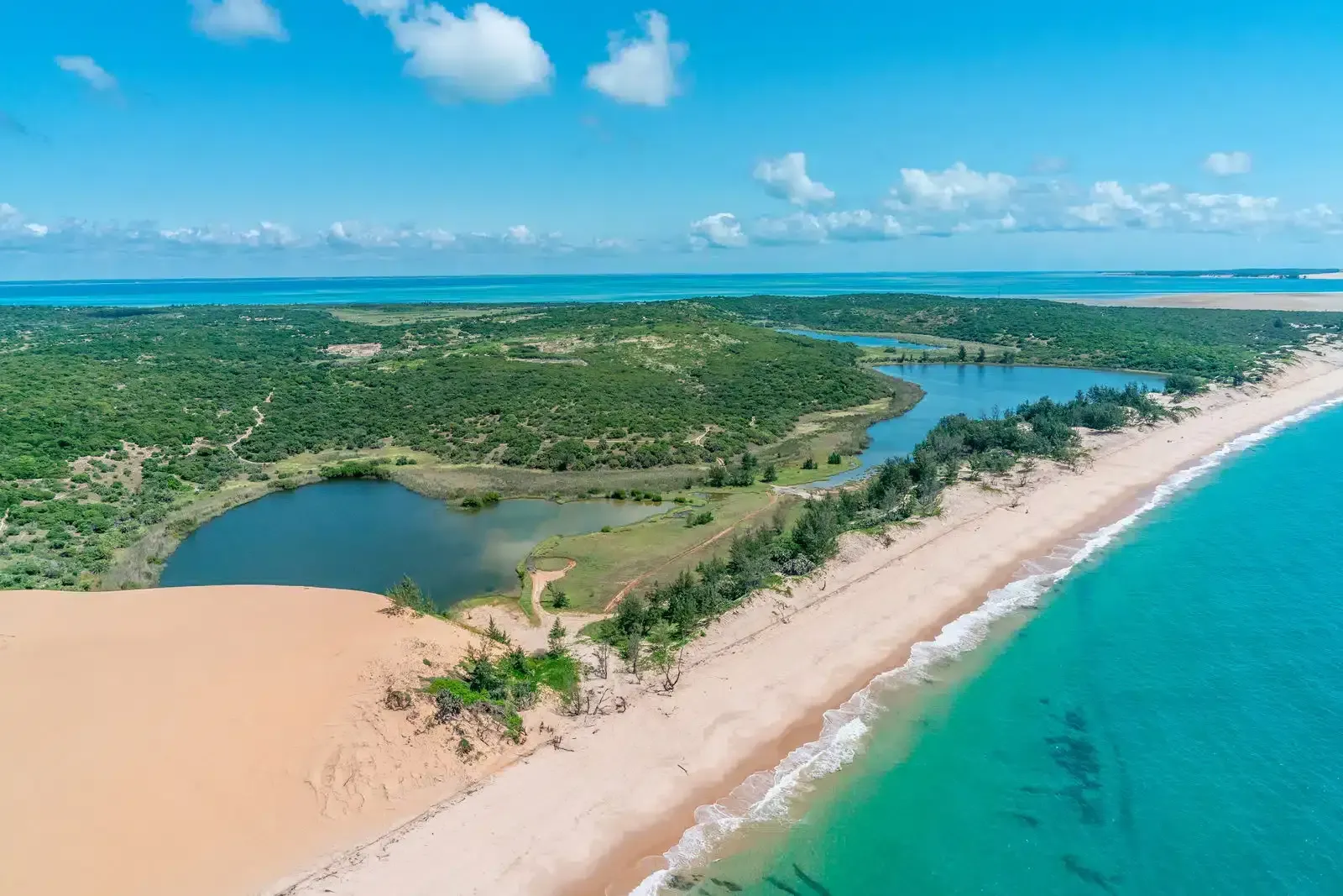 Aerial view of a tropical coastline with turquoise water, sandy beach, and green wetlands under a blue sky