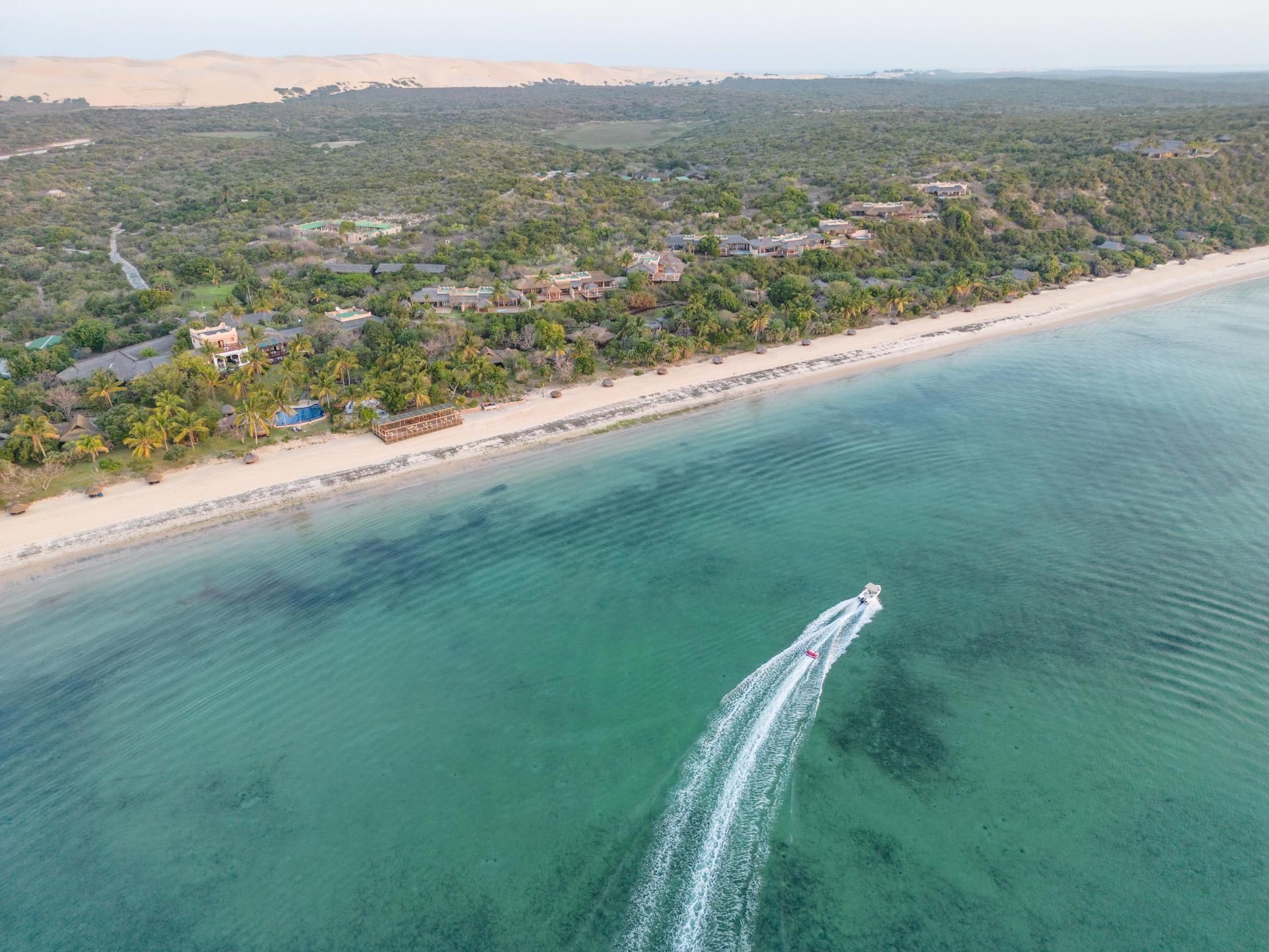 Aerial view of a tropical beach with turquoise water, white sand, and a speedboat leaving a wake.