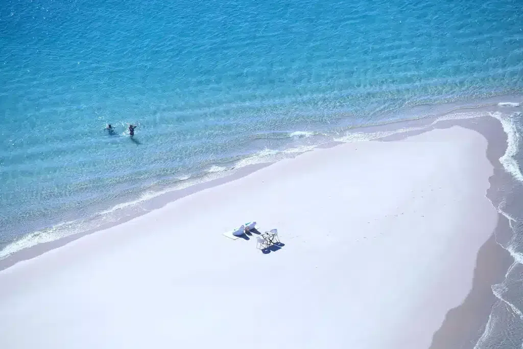 Aerial view of a white sand beach with turquoise water and a few people near the shoreline