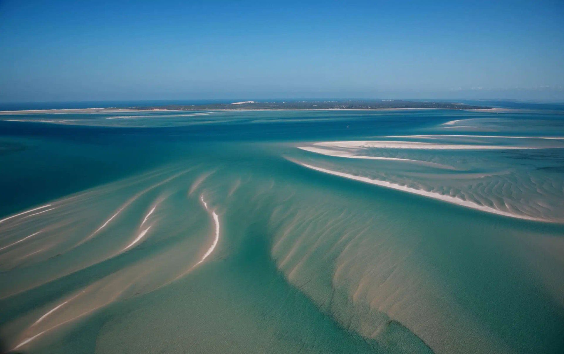 Aerial view of turquoise tidal flats with sandbars and rippling shallow water.