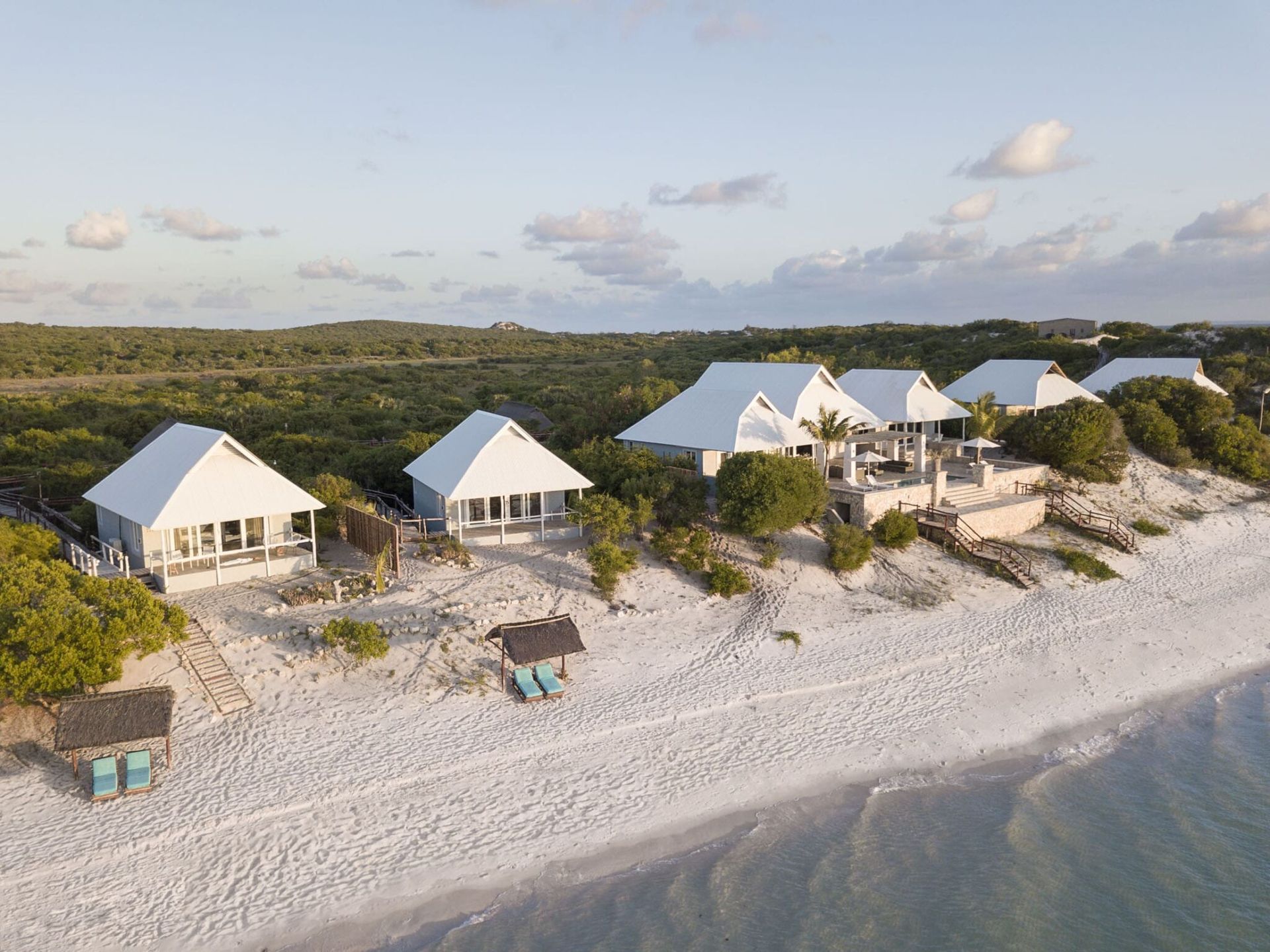 White beach cottages and cabanas beside a sandy shoreline under a clear sky.