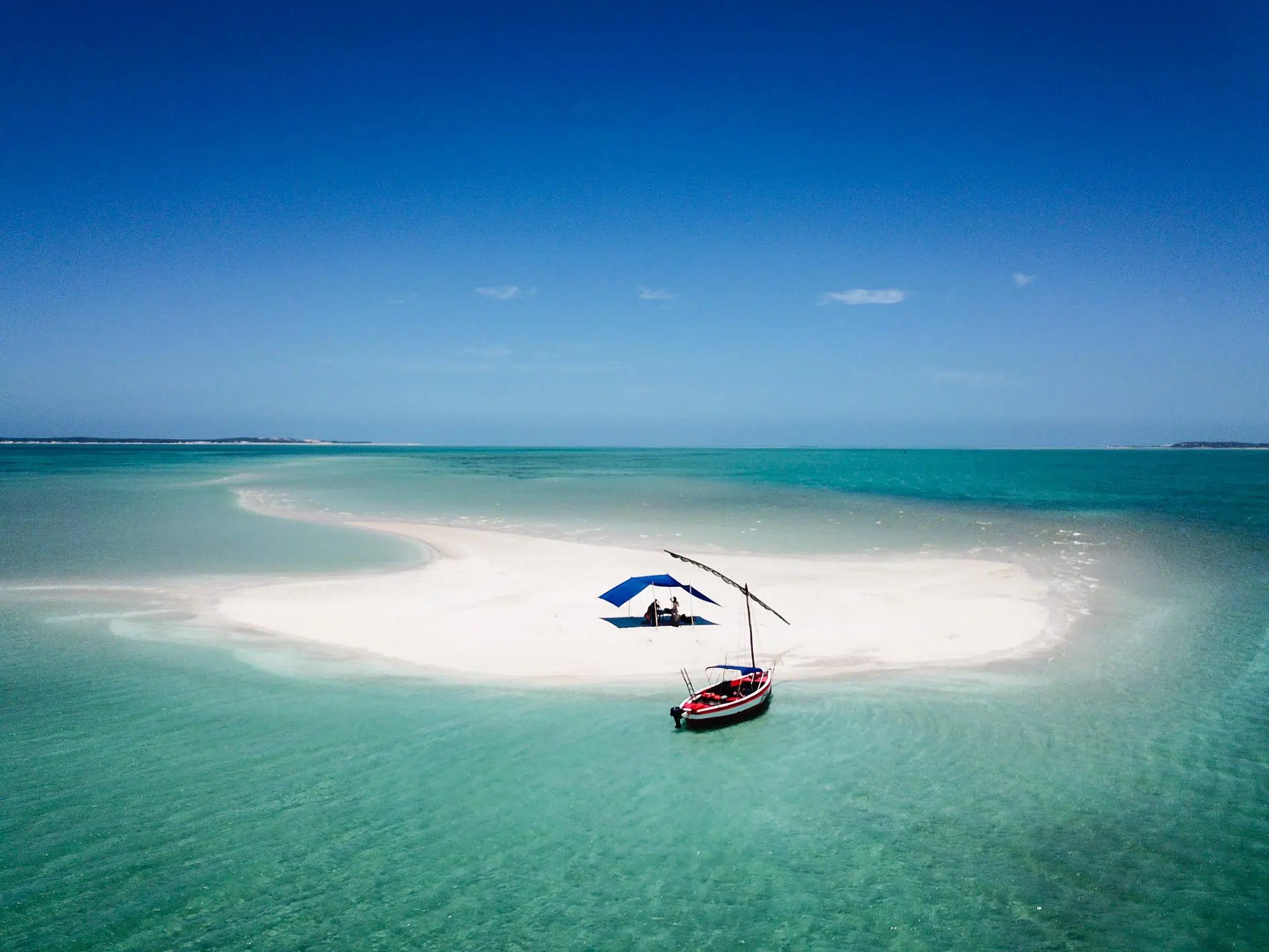 Two small sailboats near a white sandbar in turquoise tropical water under a clear blue sky