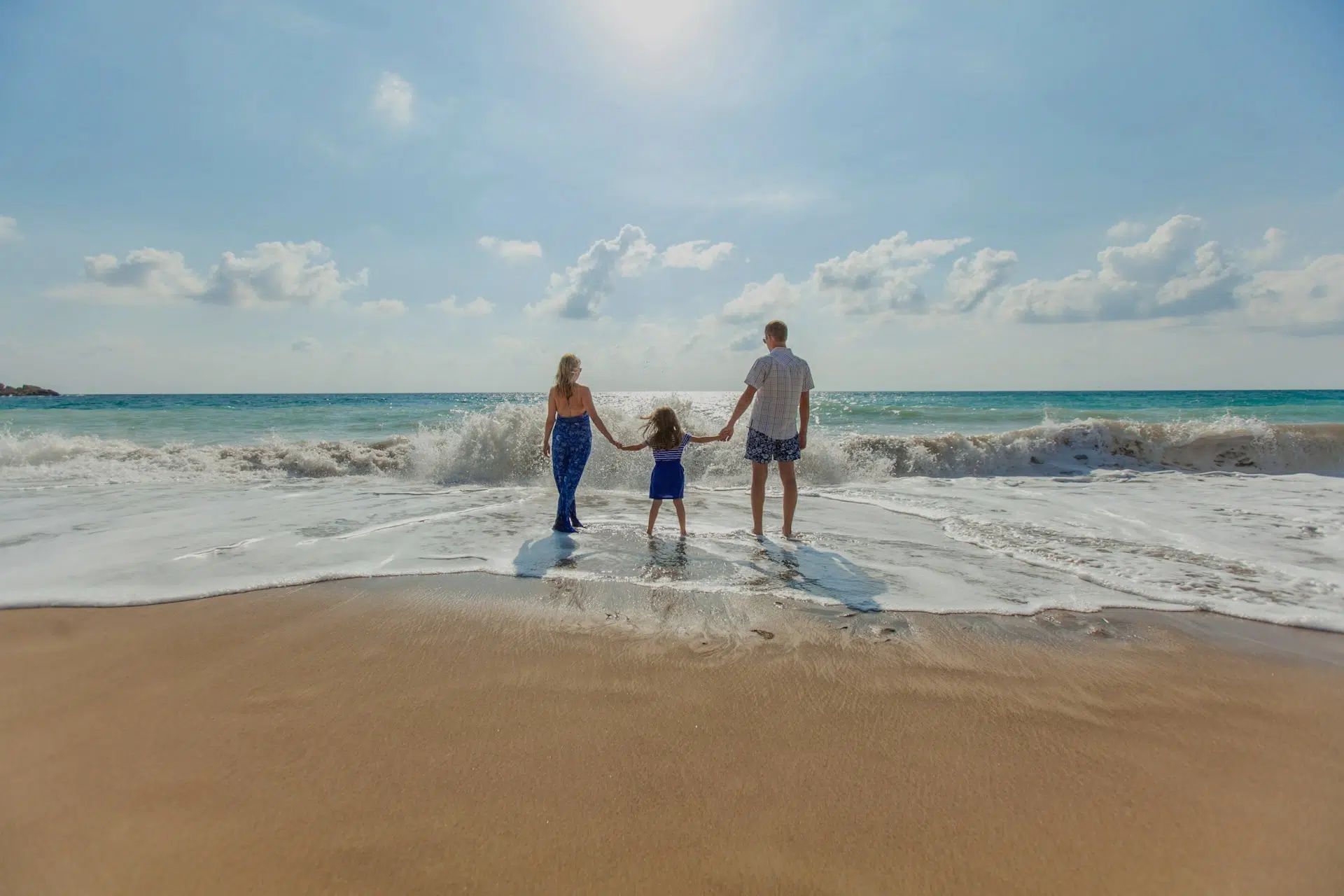 Three people holding hands walking into shallow ocean waves on a sunny beach