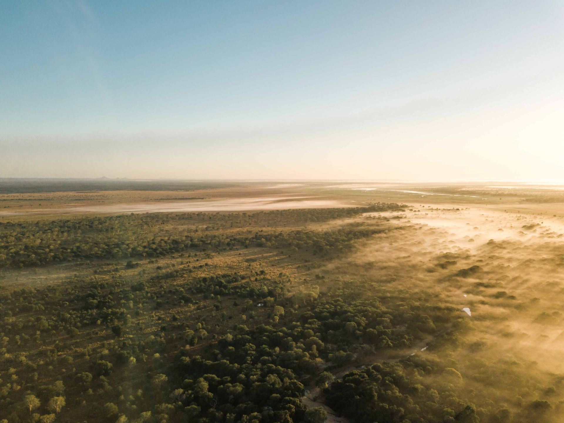 Aerial view of a sunlit, green landscape with open plains and a hazy horizon