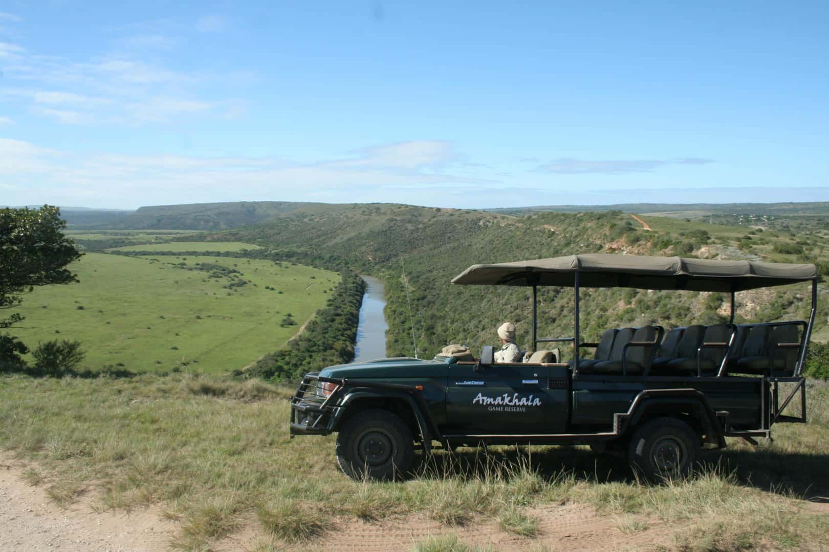 Safari vehicle overlooking a green valley and winding river under a blue sky