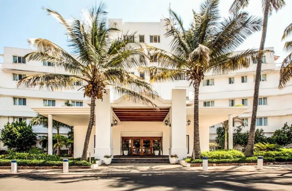 Modern white hotel entrance with palm trees and a shaded driveway