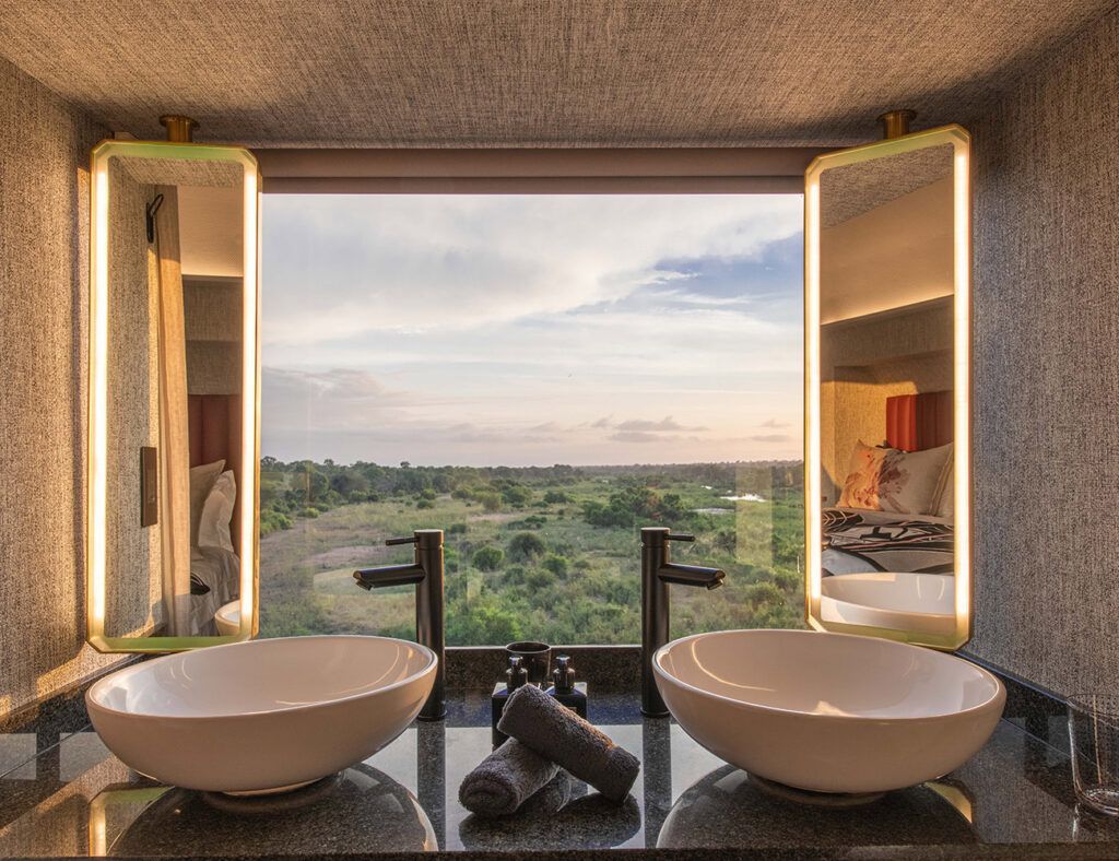 Spa bathroom with twin sinks and open windows overlooking a green landscape at sunset