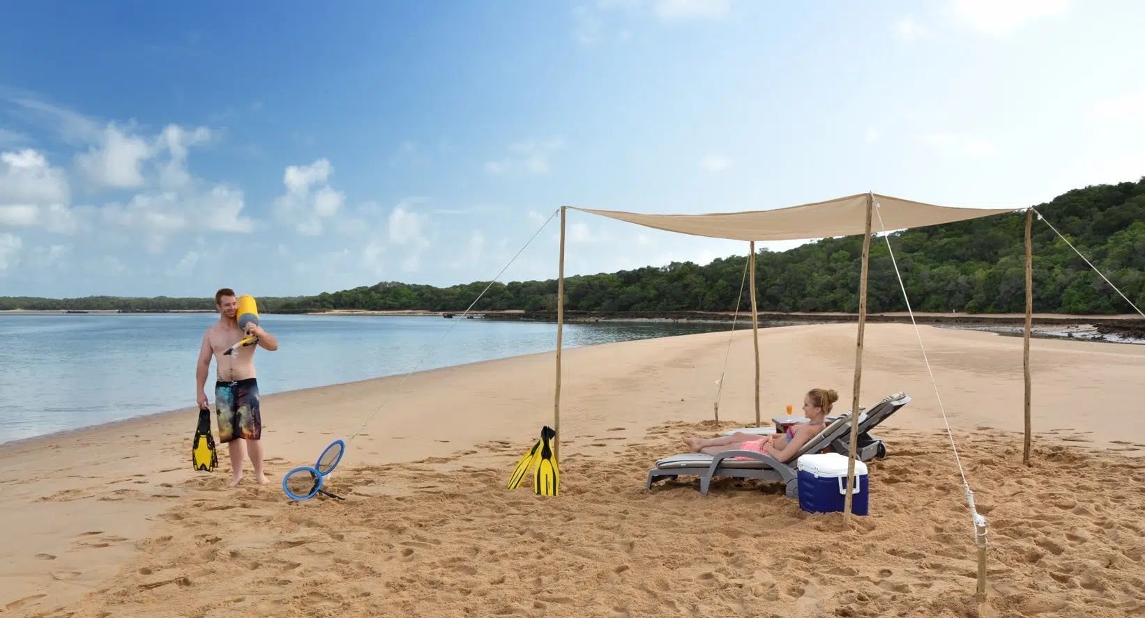Beach shade canopy with two lounge chairs, cooler, and a person walking by the water.