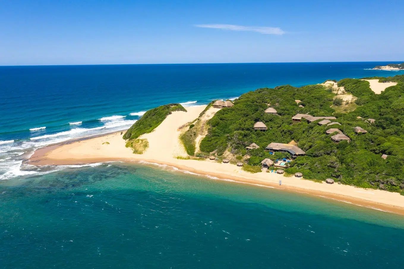 Aerial view of a sandy tropical island with turquoise water, green vegetation, and small thatched huts