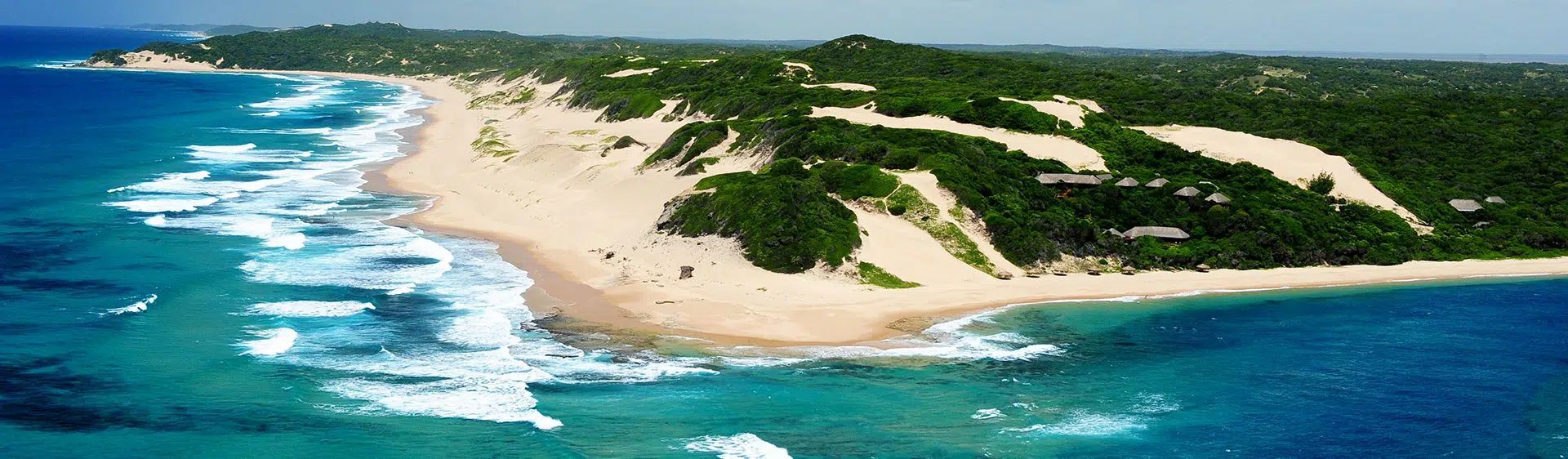 Aerial view of a sandy beach with turquoise ocean waves and green vegetation on a coastal peninsula