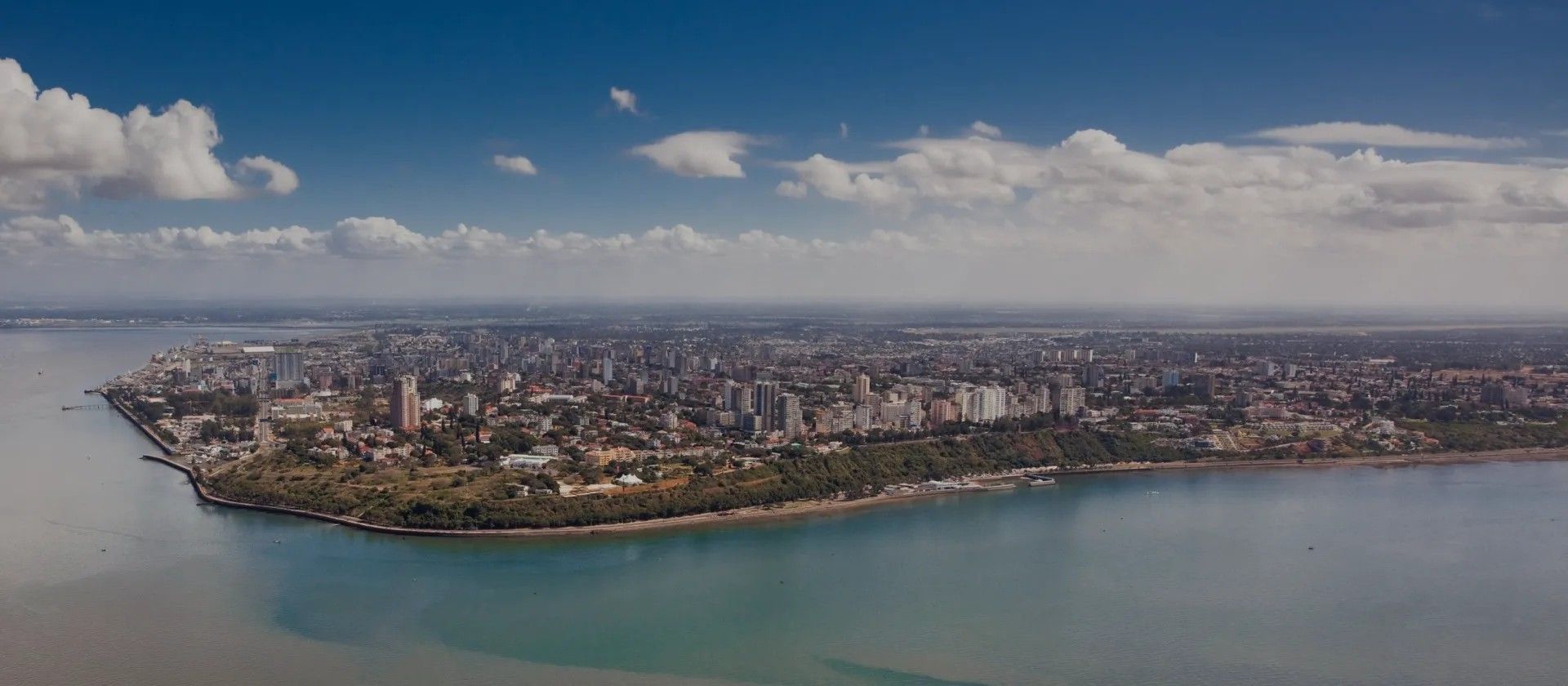 Aerial view of a coastal city skyline beside a wide blue bay under a partly cloudy sky