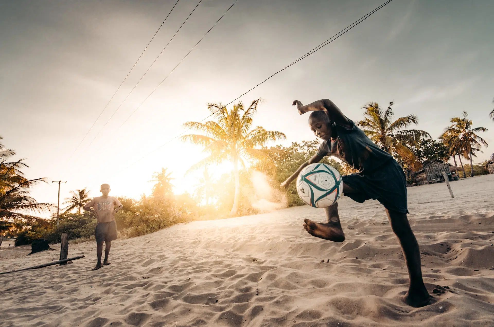 Beach soccer players kicking a ball at sunset with palm trees in the background