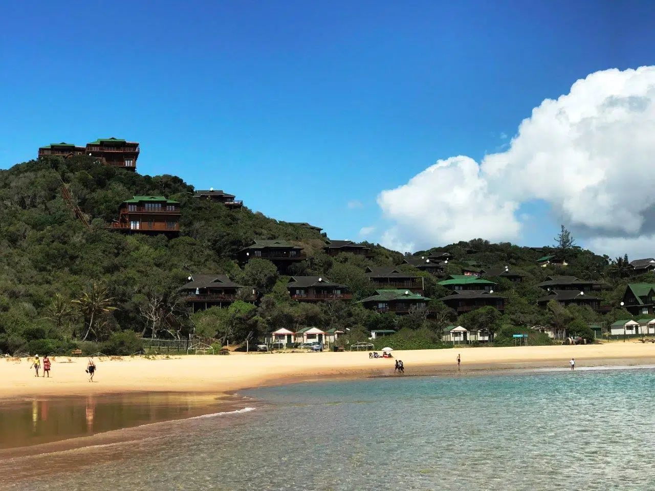 Sunlit tropical beach with sandy shore, turquoise water, and green hillside under a blue sky