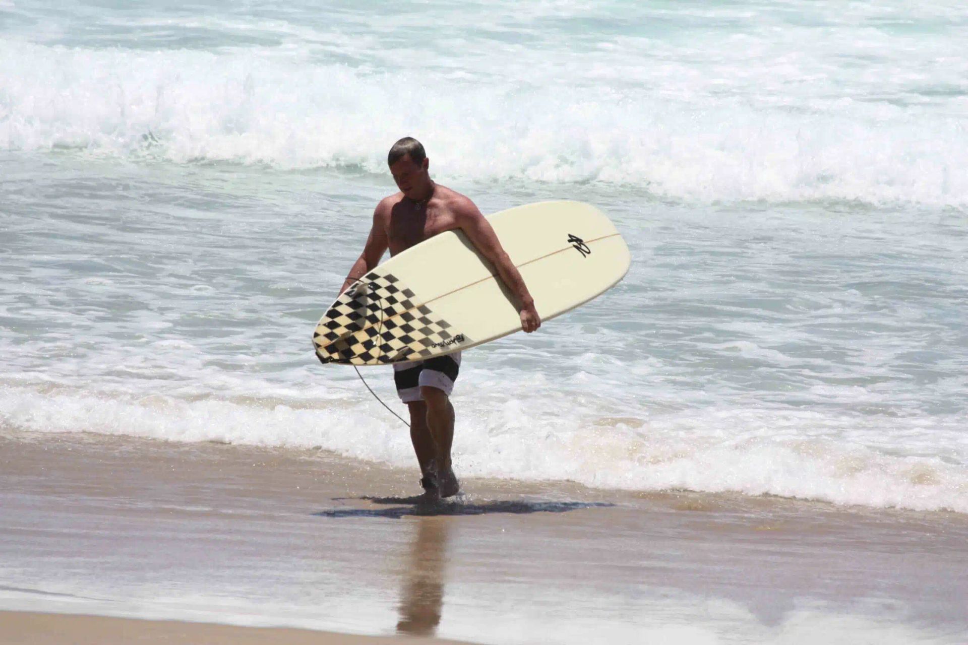 Surfer carrying a surfboard at the shoreline with waves crashing behind him