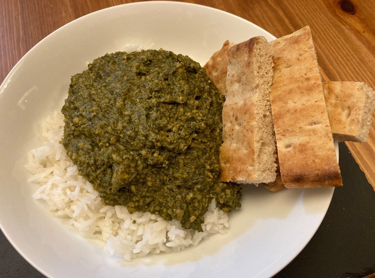 Plate of white rice topped with green curry, with pieces of flatbread on the side.