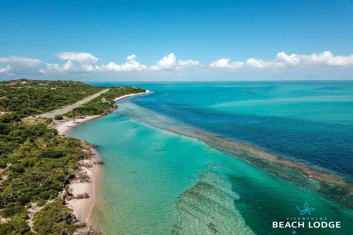 Aerial view of a turquoise tropical bay beside a green coastline under a blue sky
