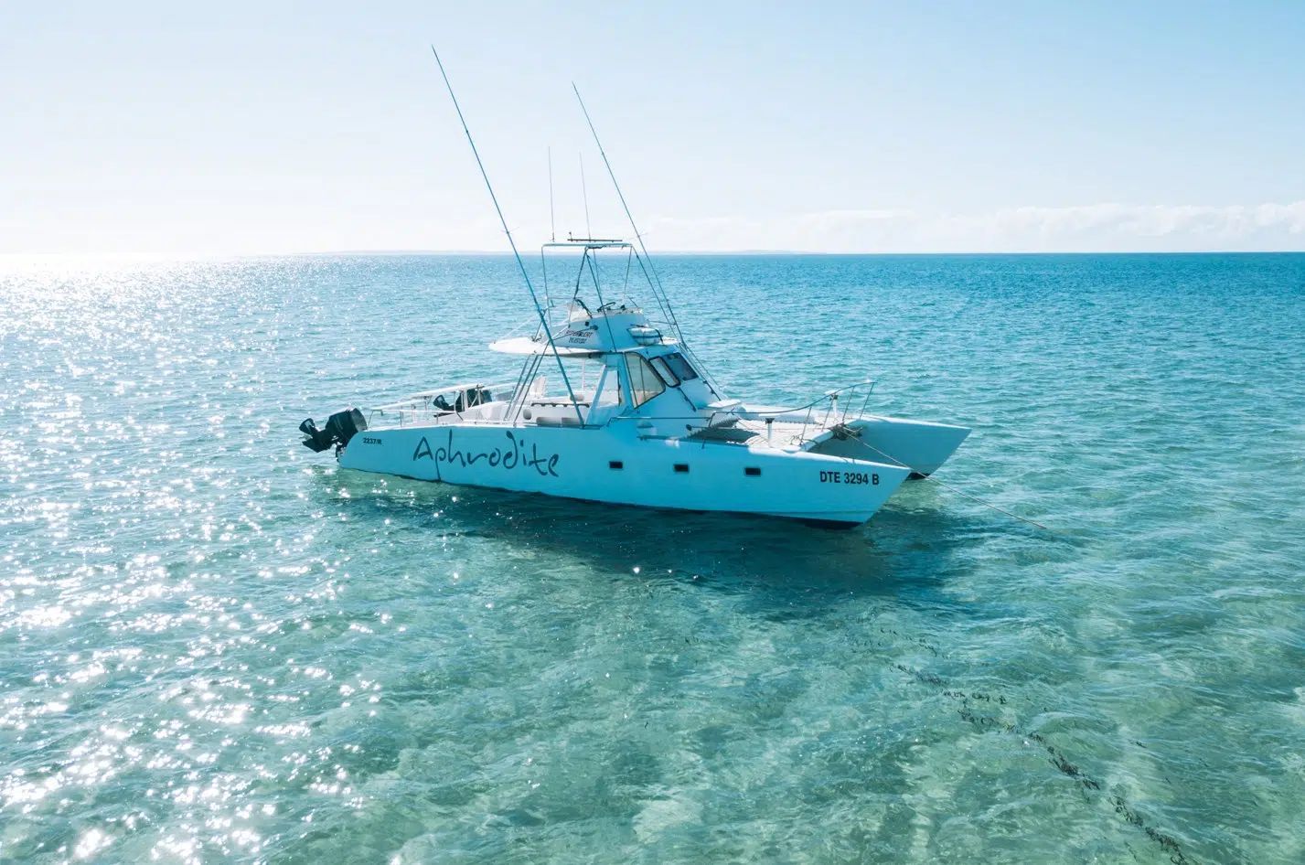 White fishing boat on clear turquoise water under a bright blue sky, seen from above