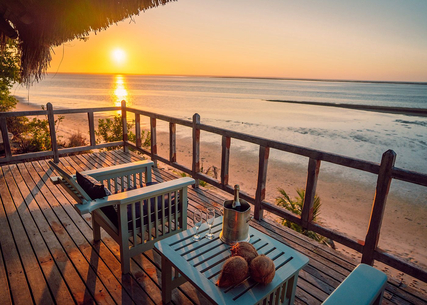 Sunset over calm beach from a wooden deck with table, chairs, and railing