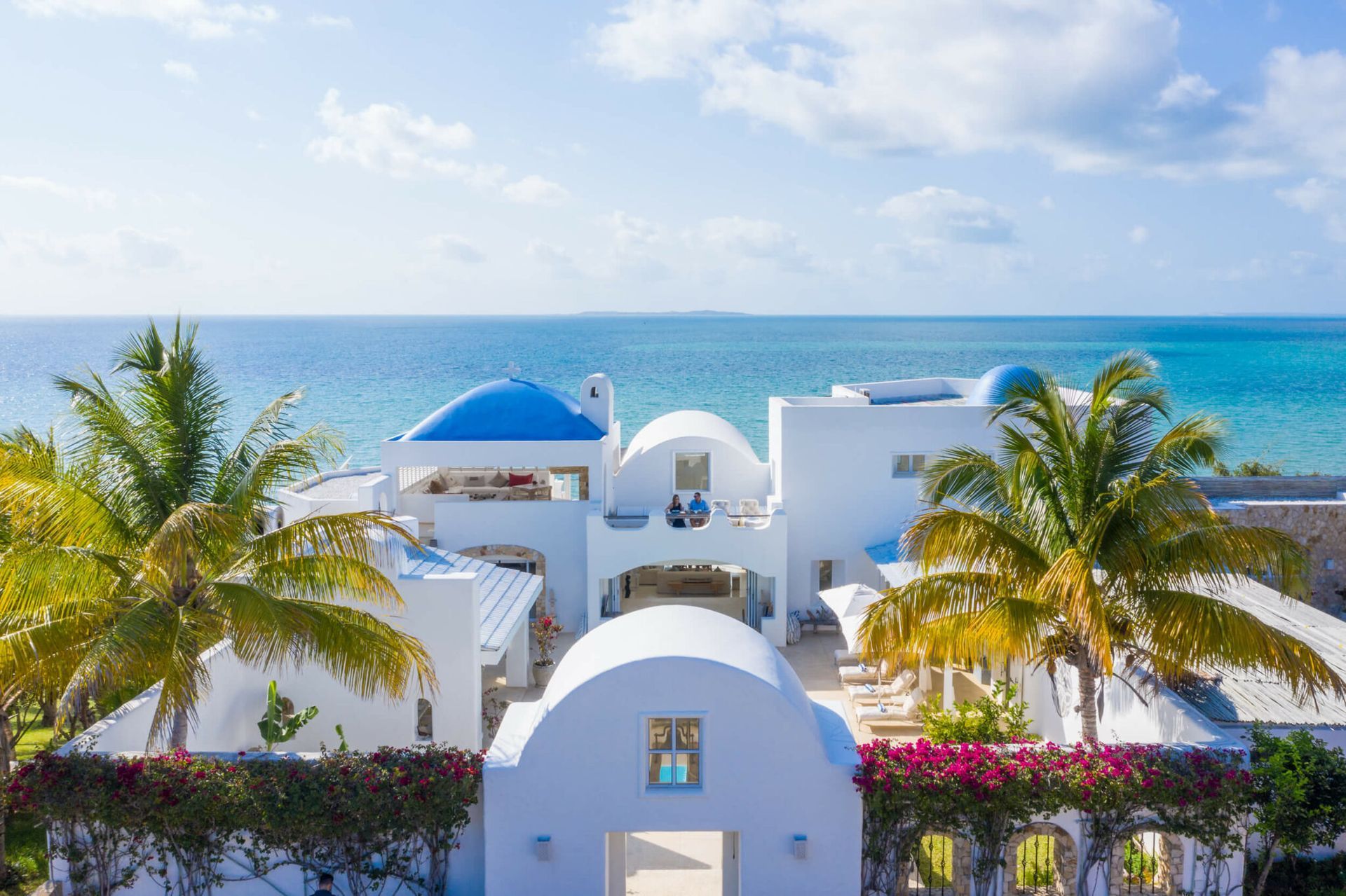 White seaside resort with blue domes, palm trees, and the ocean beyond under a bright sky