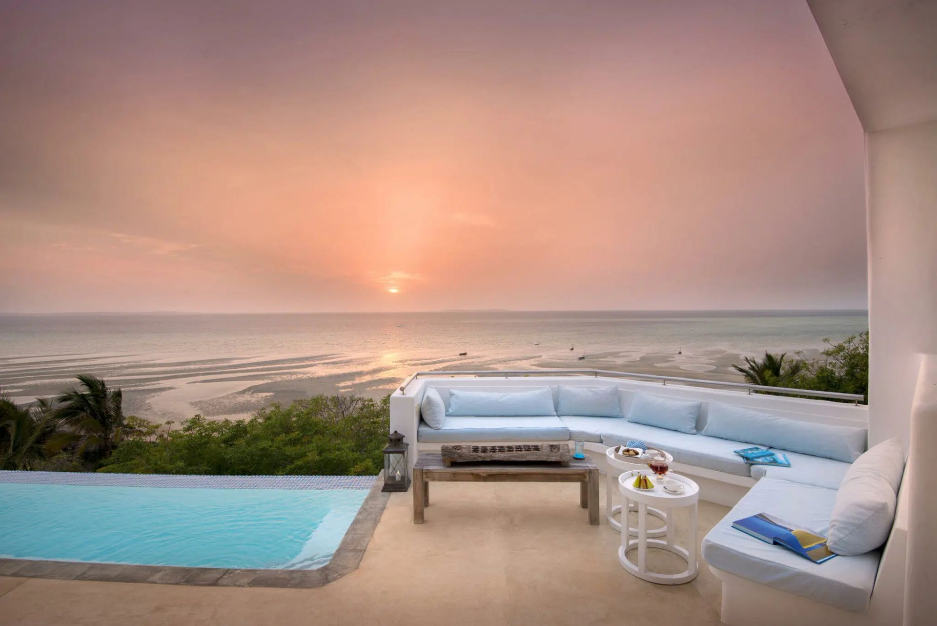 Oceanfront patio with white sectional, pool, and sunset over the sea