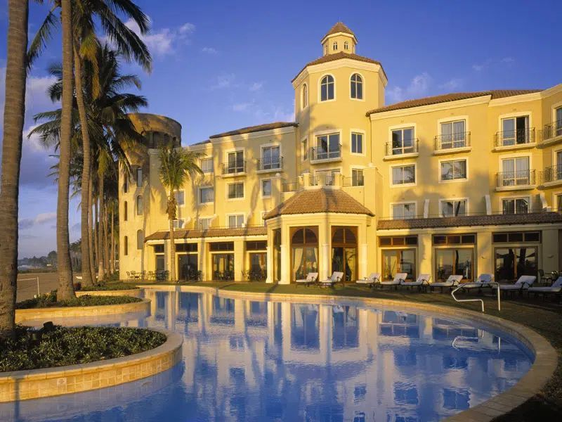 Yellow resort hotel with a curved pool and palm trees at sunset