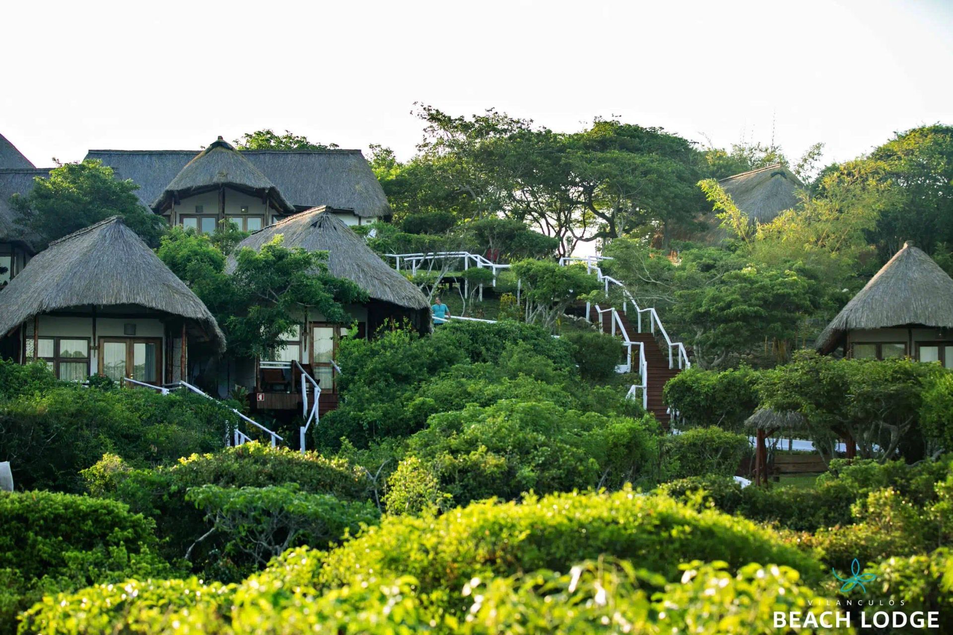 Lush hillside resort with thatched-roof cottages, winding paths, and dense green foliage