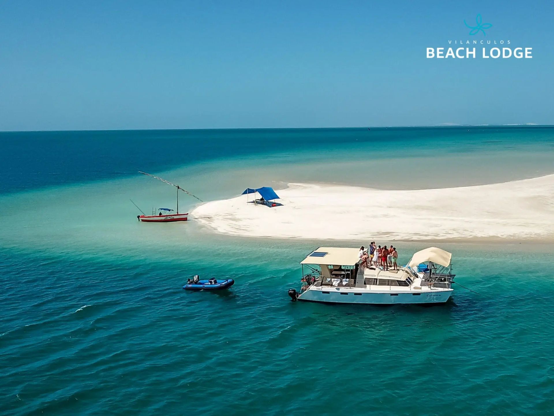 Turquoise sea with sandbar, small boats, and a beach lodge on a tropical island