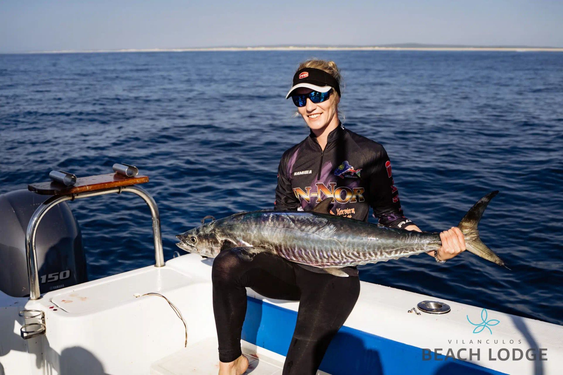 Person on a boat holding a large fish on open water under a clear sky.